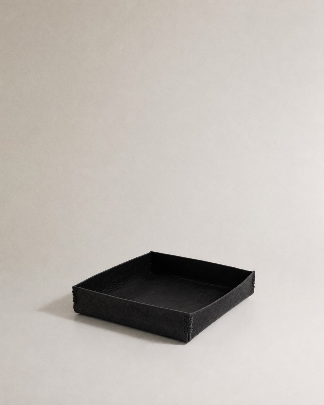 A shallow square tray in blackened leather with stitched corners.